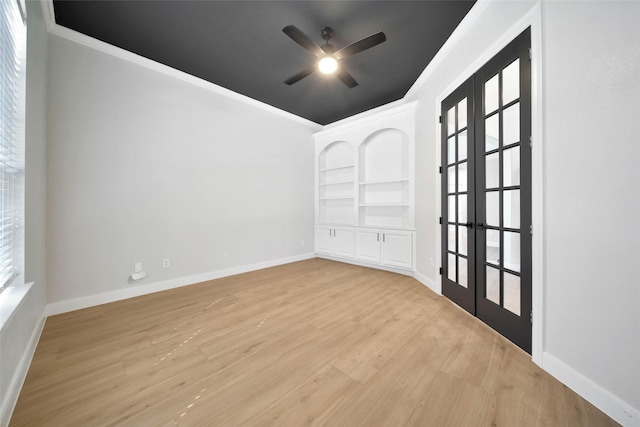 empty room featuring baseboards, a ceiling fan, ornamental molding, light wood-type flooring, and built in shelves