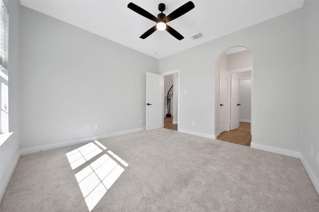 unfurnished bedroom with carpet, visible vents, arched walkways, and baseboards