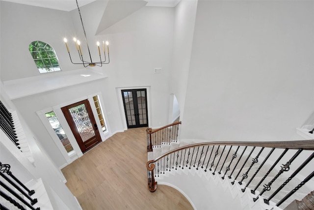 foyer entrance featuring a notable chandelier, a towering ceiling, light wood-style floors, french doors, and stairway