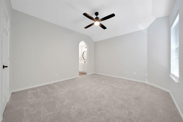 carpeted spare room featuring lofted ceiling, baseboards, arched walkways, and ceiling fan