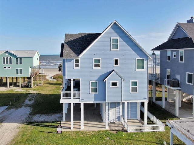 back of house featuring a balcony, a water view, a yard, roof with shingles, and a patio area