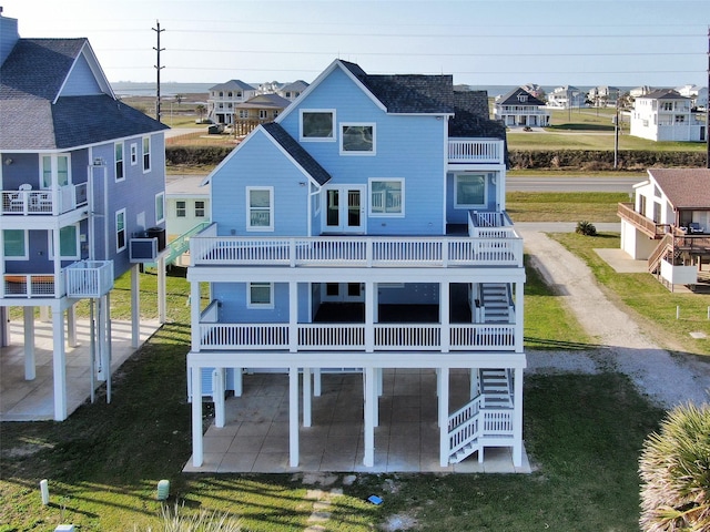 rear view of property with dirt driveway, a lawn, a patio area, a balcony, and stairs