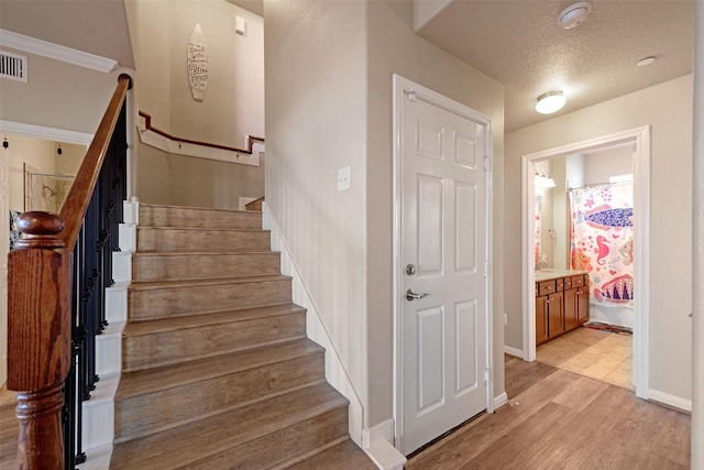 staircase with a textured ceiling, wood finished floors, and baseboards