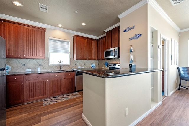 kitchen featuring light wood finished floors, visible vents, dark countertops, stainless steel appliances, and a sink