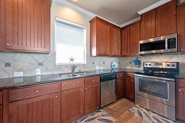 kitchen with light wood finished floors, dark stone counters, stainless steel appliances, crown molding, and a sink