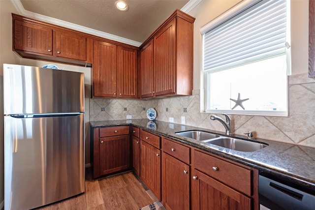 kitchen with a sink, freestanding refrigerator, brown cabinets, light wood finished floors, and dark stone countertops