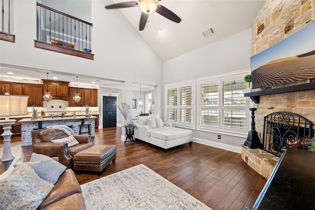 living room featuring a stone fireplace, dark wood-style flooring, visible vents, and baseboards