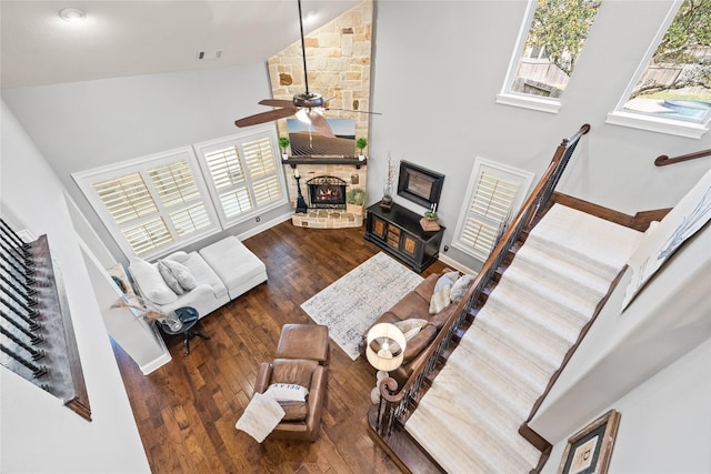 living room with visible vents, wood-type flooring, ceiling fan, a stone fireplace, and high vaulted ceiling