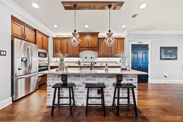 kitchen featuring light stone counters, brown cabinets, a center island with sink, stainless steel appliances, and a sink