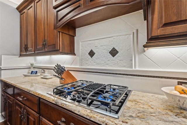 kitchen featuring black gas cooktop, backsplash, and light stone counters