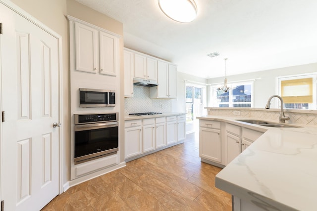 kitchen featuring under cabinet range hood, stainless steel appliances, a sink, visible vents, and decorative backsplash