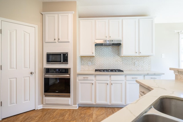 kitchen with under cabinet range hood, tasteful backsplash, white cabinetry, and stainless steel appliances