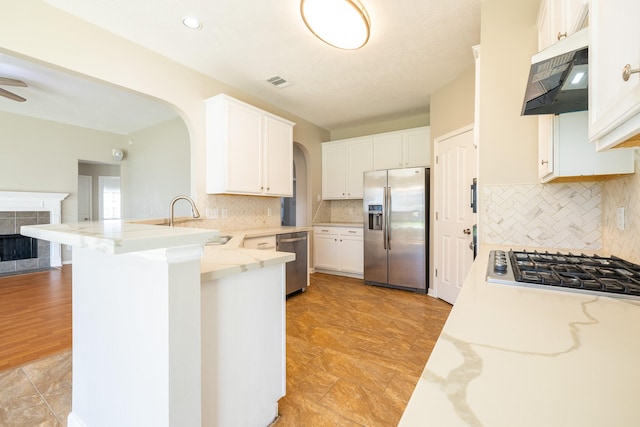 kitchen with under cabinet range hood, stainless steel appliances, a peninsula, a sink, and visible vents