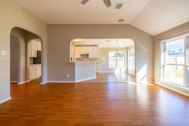 unfurnished living room featuring lofted ceiling, visible vents, wood finished floors, baseboards, and ceiling fan with notable chandelier