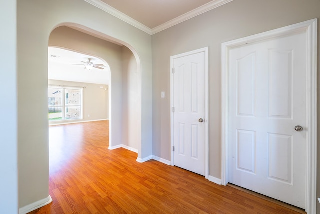 corridor featuring light wood-style flooring, arched walkways, baseboards, and ornamental molding