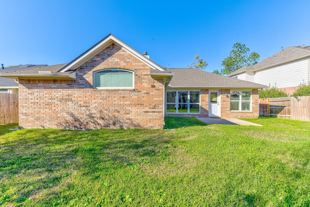 rear view of house with roof with shingles, brick siding, a yard, and fence