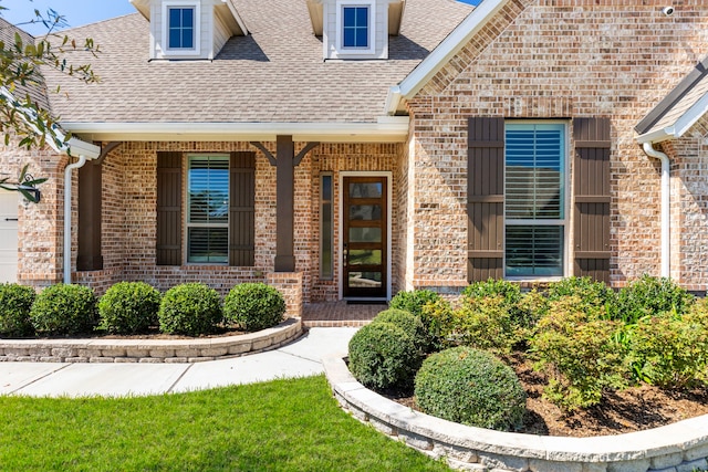 entrance to property with brick siding, a porch, and a shingled roof