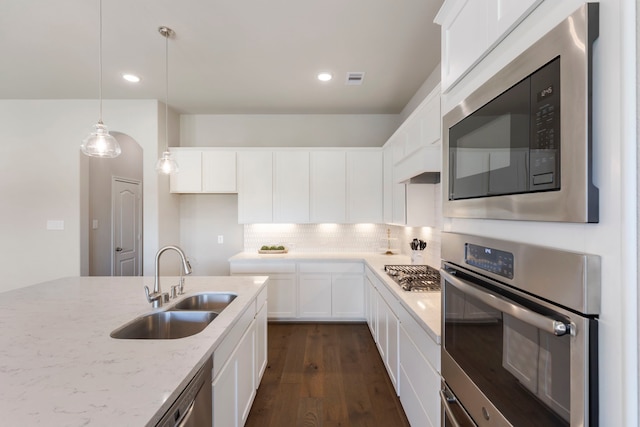 kitchen featuring light stone counters, dark wood finished floors, a sink, appliances with stainless steel finishes, and tasteful backsplash