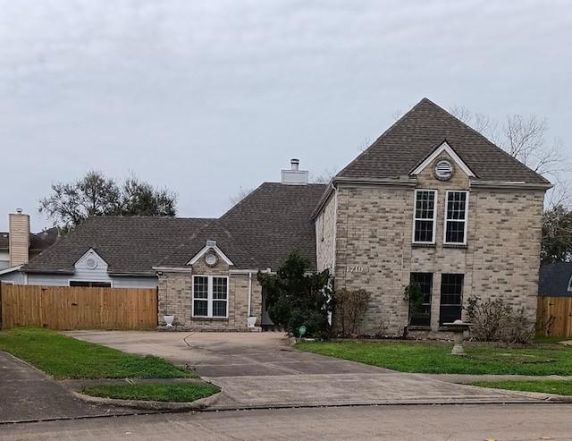 traditional-style home with driveway, brick siding, fence, and a chimney