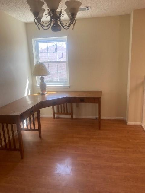 unfurnished dining area with light wood-style flooring, a textured ceiling, visible vents, and a notable chandelier