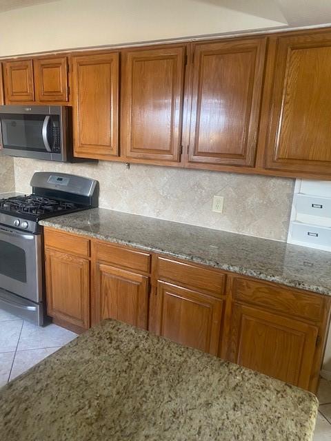 kitchen with tasteful backsplash, stone countertops, appliances with stainless steel finishes, and brown cabinetry