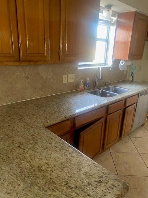 kitchen with light tile patterned floors, tasteful backsplash, brown cabinetry, a sink, and light stone countertops