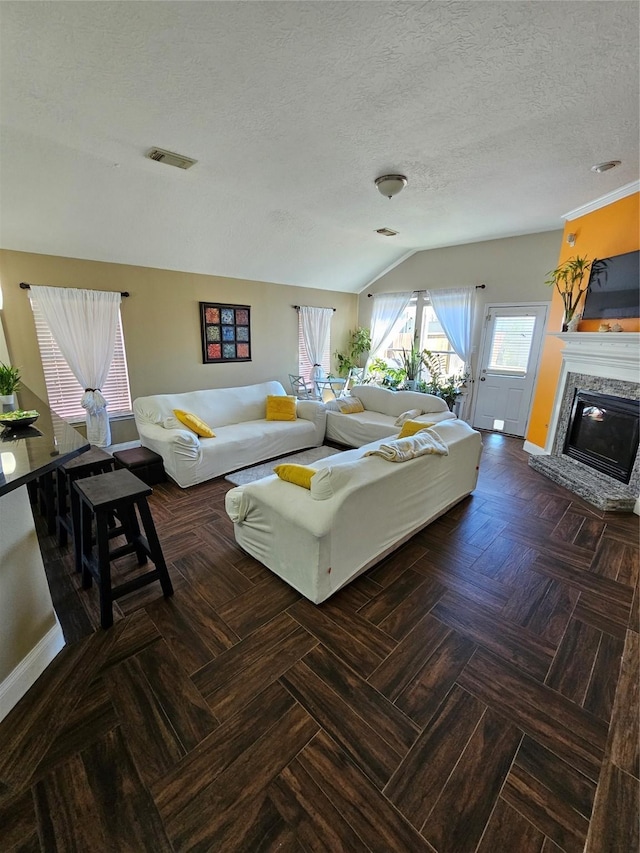 living room featuring a textured ceiling, visible vents, baseboards, vaulted ceiling, and a glass covered fireplace