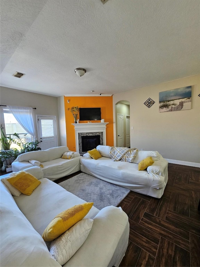 living room with arched walkways, visible vents, a premium fireplace, a textured ceiling, and baseboards