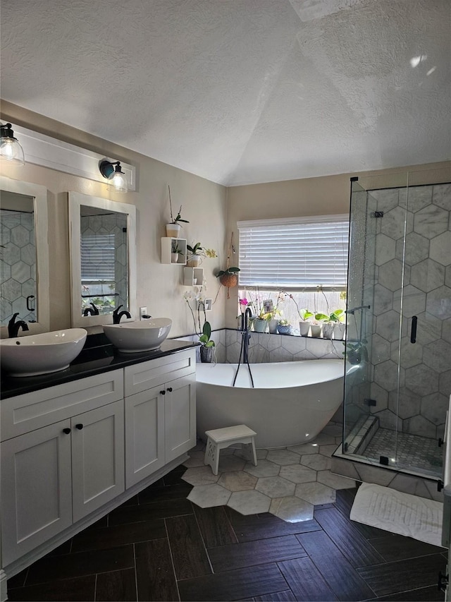 bathroom with a textured ceiling, a freestanding tub, a stall shower, and a sink