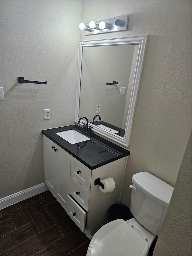 half bathroom featuring baseboards, a textured wall, vanity, and toilet