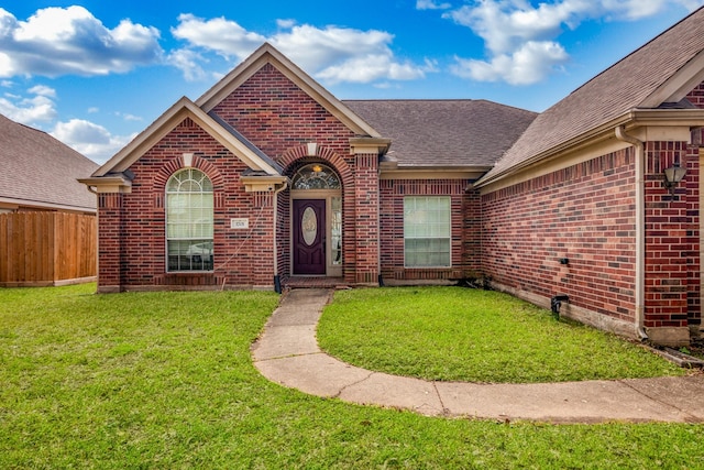 view of front of property with a shingled roof, a front yard, brick siding, and fence