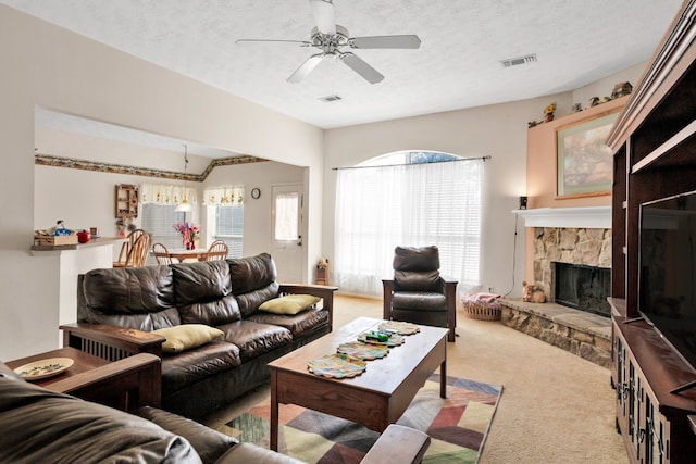 living area with visible vents, ceiling fan, carpet, a textured ceiling, and a stone fireplace