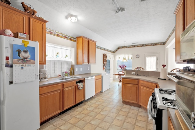 kitchen featuring a textured ceiling, a peninsula, white appliances, a sink, and light countertops