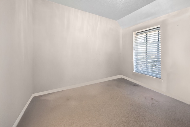 empty room with a textured ceiling, lofted ceiling, and baseboards