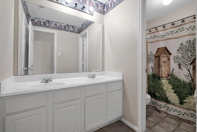 bathroom with toilet, double vanity, baseboards, and a sink