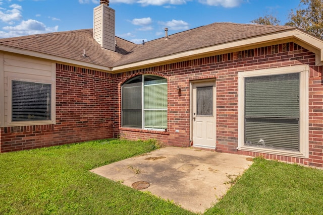 rear view of house with brick siding, a yard, roof with shingles, a chimney, and a patio area