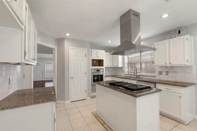 kitchen featuring island exhaust hood, appliances with stainless steel finishes, light tile patterned flooring, a sink, and dark stone counters