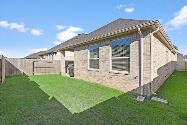 rear view of house featuring a fenced backyard, roof with shingles, a lawn, and brick siding