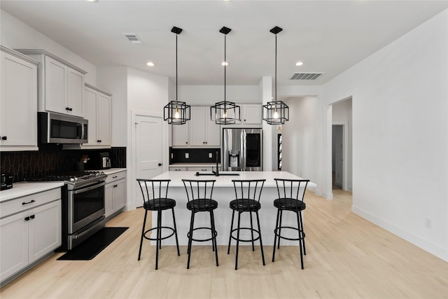 kitchen featuring a kitchen breakfast bar, appliances with stainless steel finishes, a center island with sink, and decorative backsplash