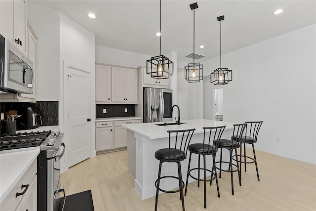 kitchen featuring white cabinets, a center island with sink, stainless steel appliances, and a sink