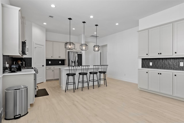 kitchen featuring a breakfast bar area, stainless steel appliances, visible vents, light countertops, and light wood-type flooring