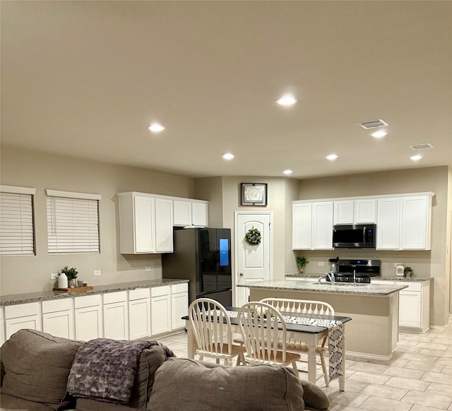 kitchen featuring visible vents, stainless steel microwave, freestanding refrigerator, white cabinets, and stove