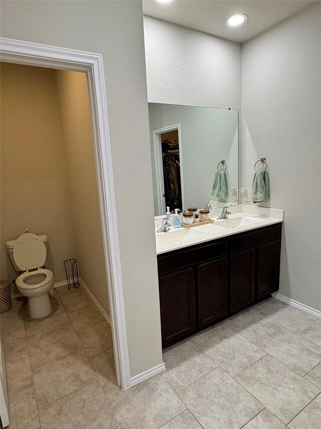 full bath featuring double vanity, a walk in closet, baseboards, and a sink