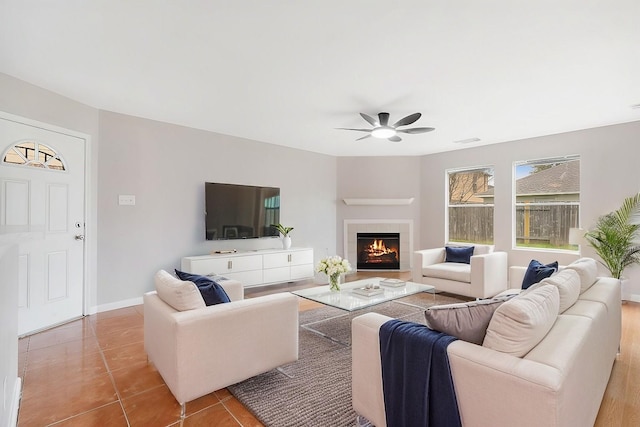 living room featuring visible vents, a tiled fireplace, light tile patterned floors, baseboards, and ceiling fan