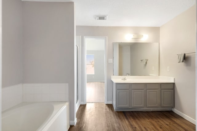 bathroom featuring visible vents, baseboards, wood finished floors, a bath, and vanity