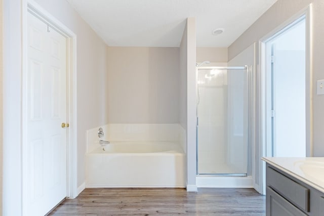 full bath featuring a shower stall, vanity, a garden tub, and wood finished floors