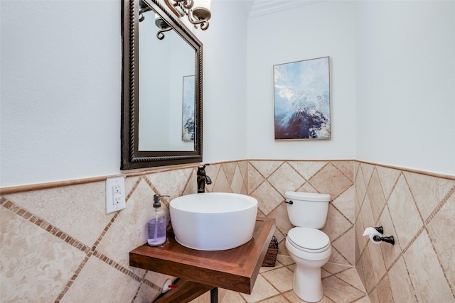 half bathroom with toilet, a wainscoted wall, tile walls, and a sink