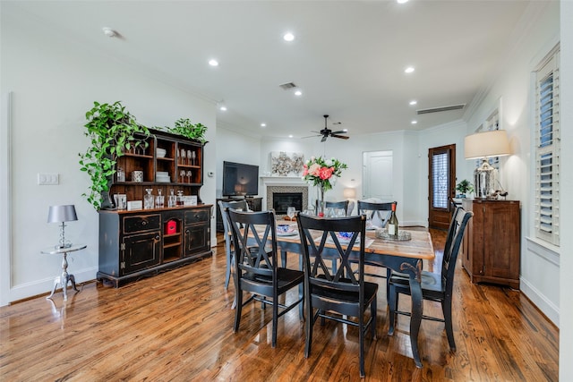 dining area with a glass covered fireplace, wood finished floors, visible vents, and crown molding