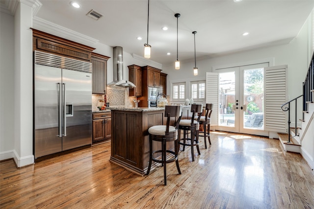 kitchen with built in appliances, visible vents, french doors, wall chimney exhaust hood, and tasteful backsplash