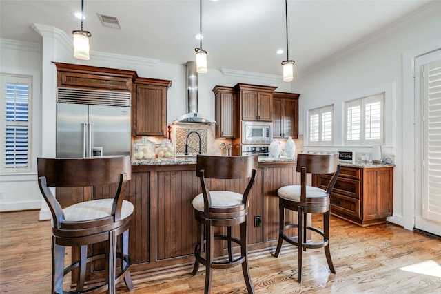 kitchen with crown molding, visible vents, decorative backsplash, built in appliances, and wall chimney exhaust hood